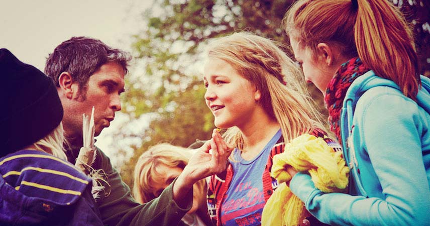 Man holding a buttercup under the chin of a guest at Bosinver as others look on smiling.