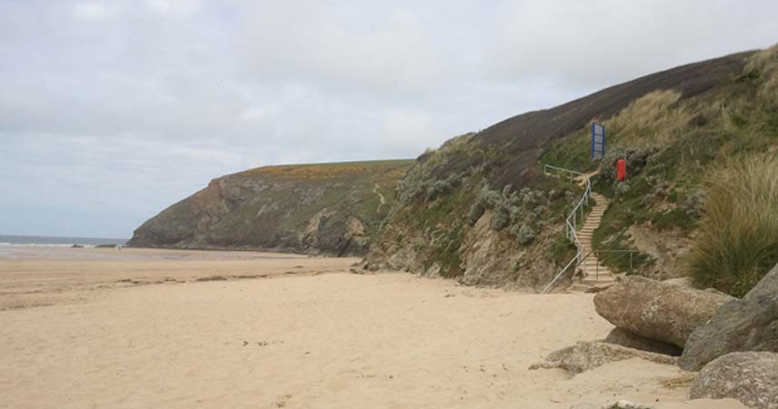Picture of the beach at Bedruthan on a grey day in Cornwall. Winding steps lead to the coast path.