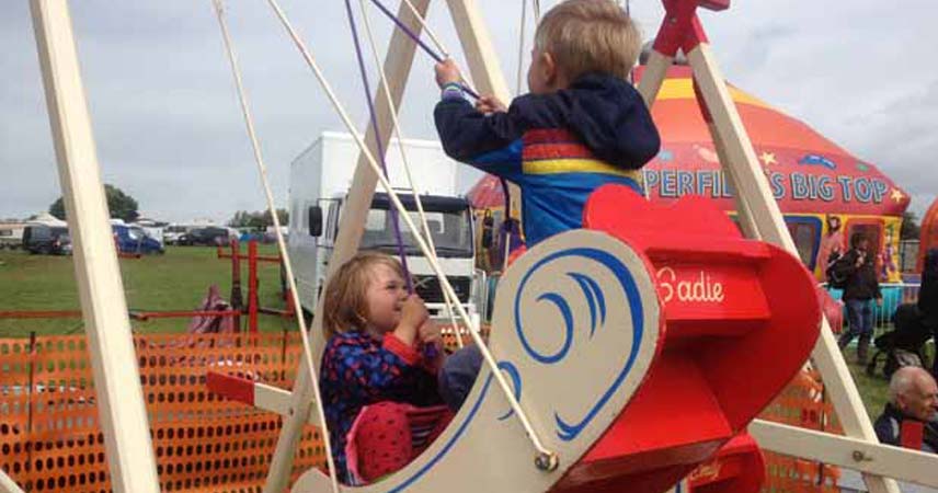 Swinging ship ride at Rock Oyster Festival. Two children laugh and smile on the ride.