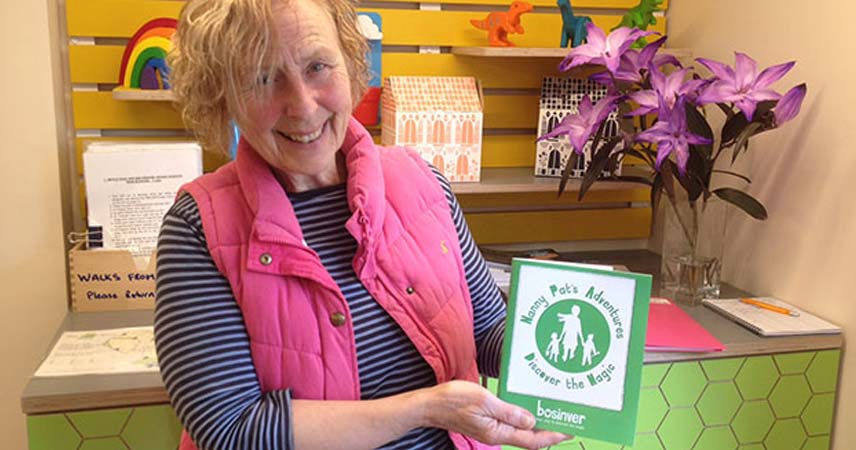 Nanny Pat in reception holding a blue book about her adventures and smiling at the camera.