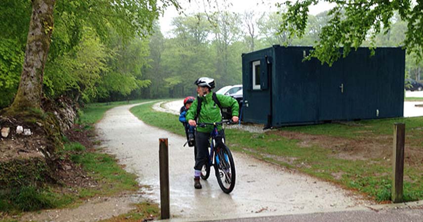 Father and son in rain coats on a bike at Lanhydrock in Cornwall on a rainy day.