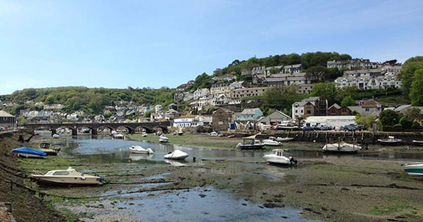 Picture of the river drained with boats beached on the riverbed, with Looe in the background.
