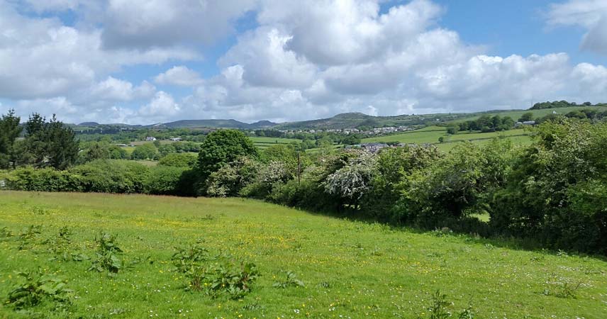 Scenic view of fields, hills and tors in Cornwall. A small town can be seen in the distance.