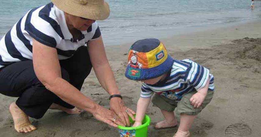 Grandma and grandchild making sandcastles with a green bucket on a sunny day.