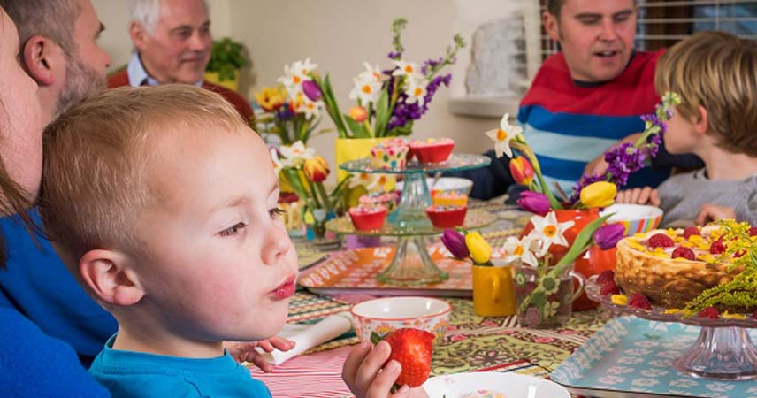 Picture of a large family eating dinner at the table at Bosinver, with a close up of a child holding a strawberry.