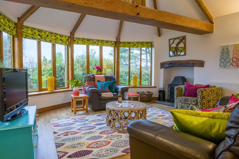 Living room area at Trerose Cottage in Bosinver, with a view of the grounds, a fire place, leather seats and a TV.