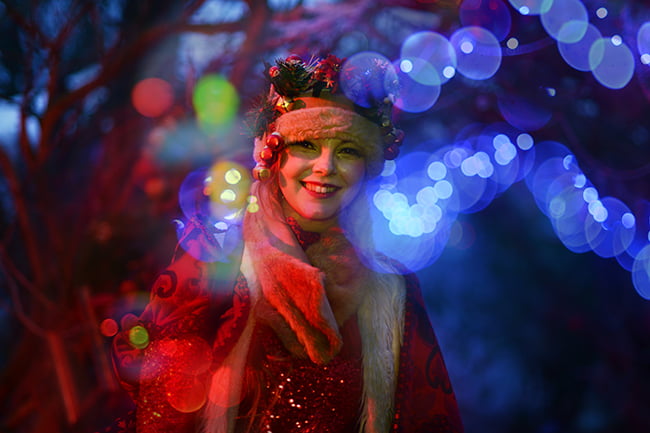 Actor from Rogue Theatre posing in the woods next to the lights.