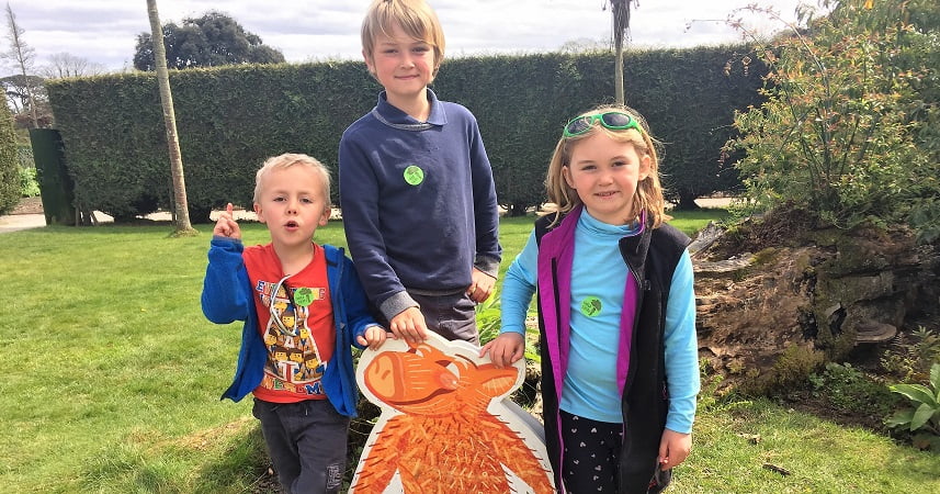 Three children at Heligan smiling for the camera next to a hedge.
