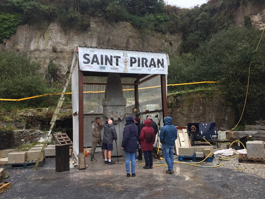 Picture of the carving of St Piran, with a host talking about the carving to a group of people.