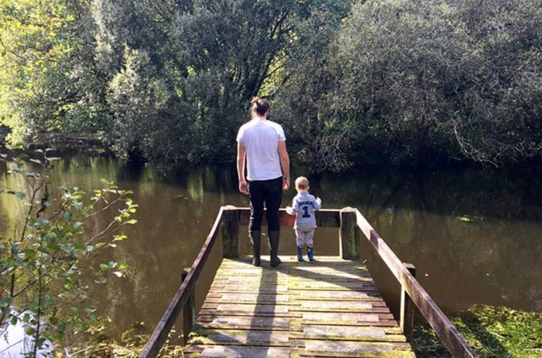 A man with a ponytail and a young boy standing on a wooden pontoon looking down at the lake at Bosinver