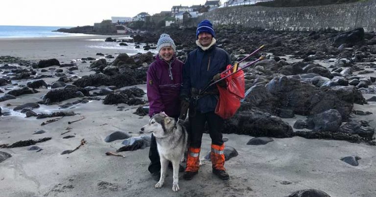 Nanny Pat with man and husky on a rocky beach holding litter picking tools.