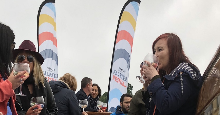 Group of people drinking gin from gin bowls in front of Fal River Festival flags