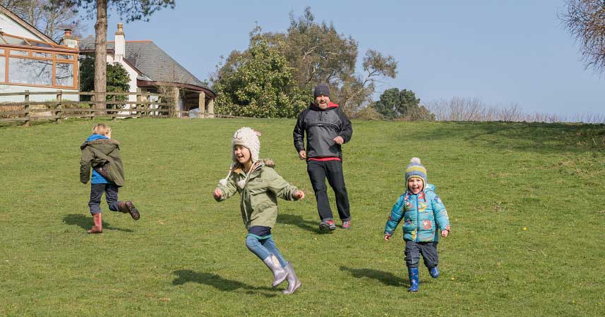 Three small children and their dad smiling and running down a grassy hill at Bosinver