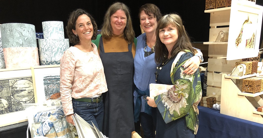 four smiling ladies hugging surrounded by art and crafts
