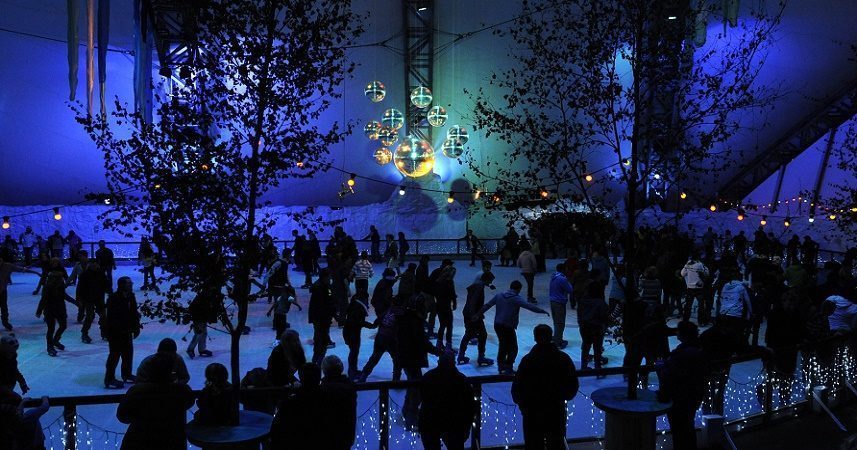 Large group of people on an ice skating rink under disco balls
