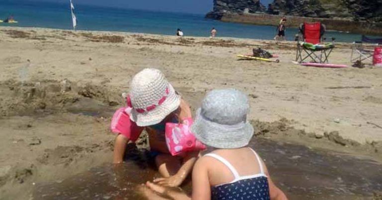 Two children playing on a beach with armbands on.