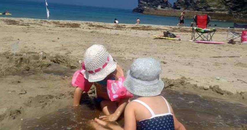 Two children playing on a beach with armbands on.