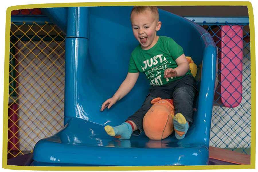 Child sliding down a blue slide whilst smiling and laughing