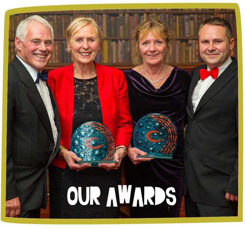 Group of four adults posing in fine clothing whilst holding an award
