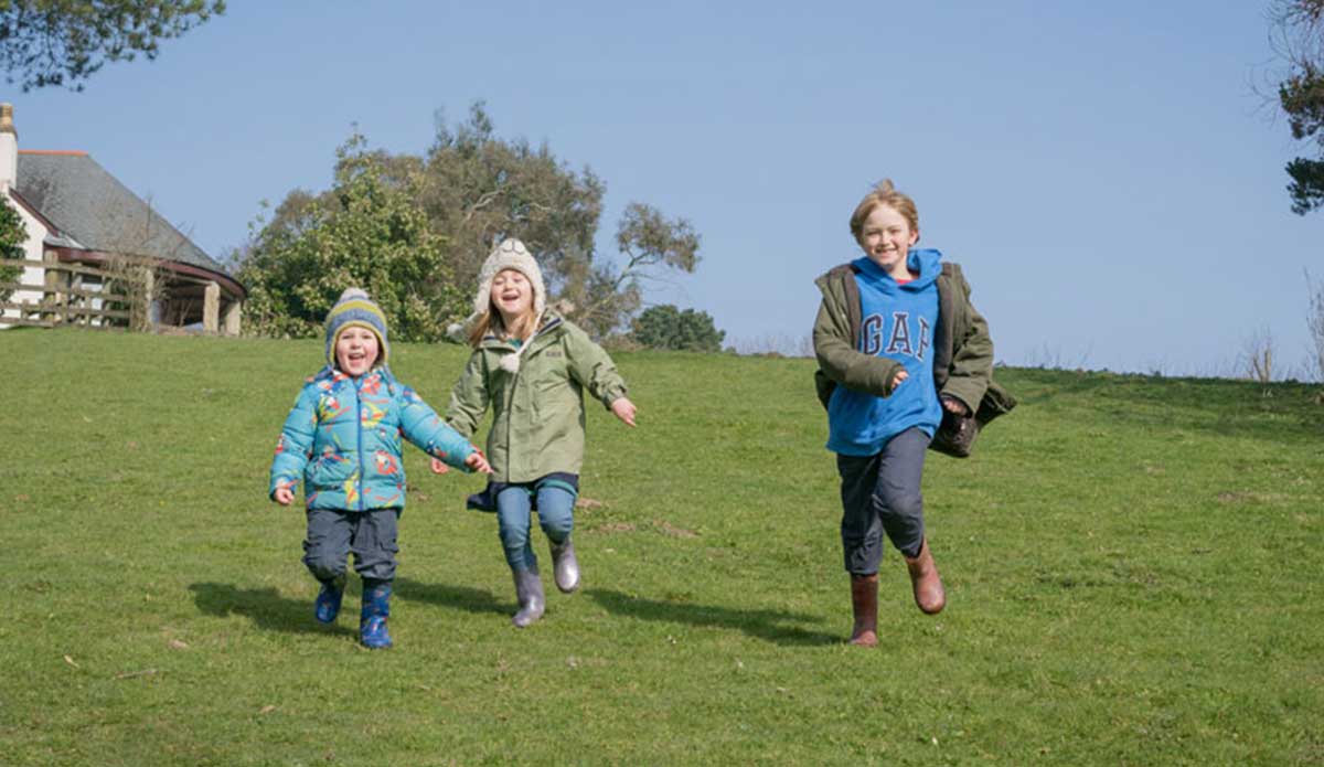 Three children wearing warm winter clothing running across a field