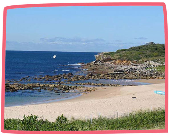 Wide shot of a sandy beach in Cornwall on a sunny day with a boat in the distance.