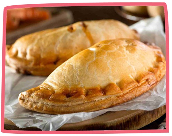 Two fresh pasties fresh out of the oven on grease proof paper.