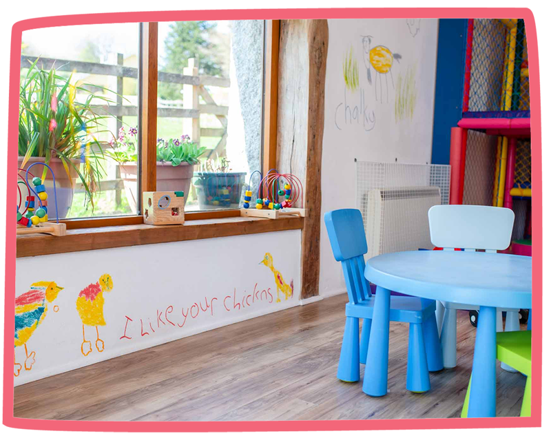 Close up of a playbarn, including a small table and chairs, toys and drawings on the walls.