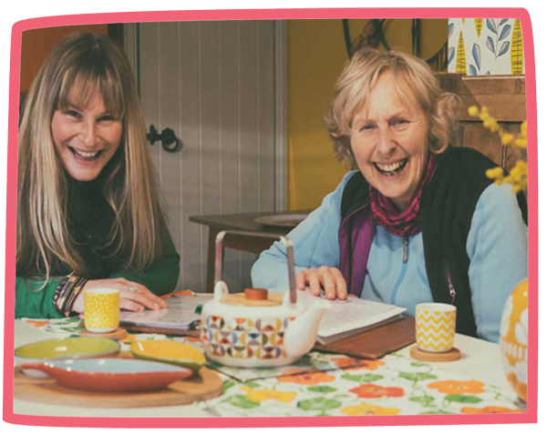 Pat and another woman drinking tea and smiling at a kitchen table at Bosinver.