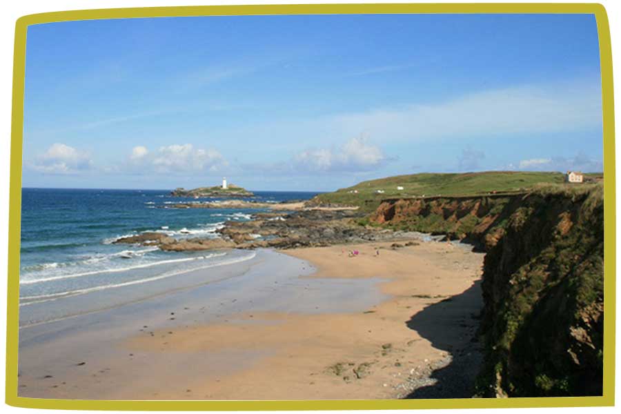 Beach in Cornwall with a small lighthouse in the distance on an offshore island.