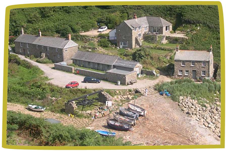 Five boats on a beach next to some small buildings by the countryside in Cornwall.