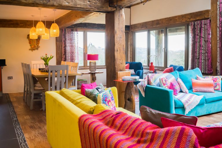 Open plan living room with colourful sofas and table with lights over in the back ground